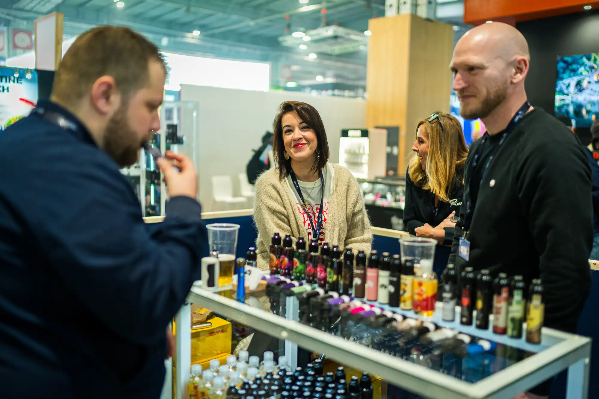 Exposants échangeant avec un visiteur en train de tester des e-liquides sur un stand du Vapexpo Paris.