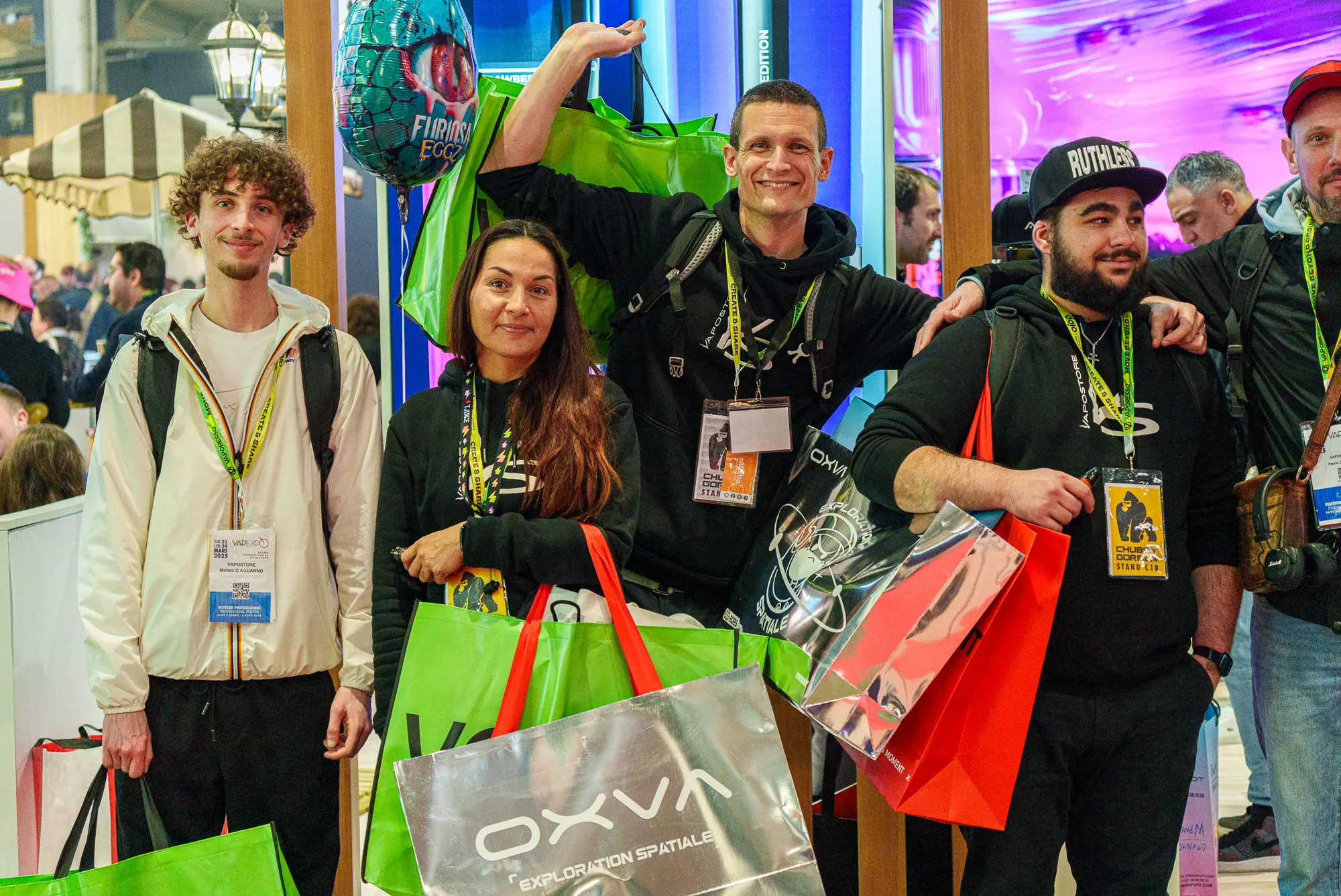 Un groupe de passionnés de la vape tout sourire affichant leurs achats lors de leur passage au salon Vapexpo Paris.